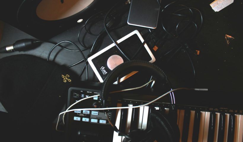 flat-lay photo of headphones, MIDI keyboard, and speaker on black surface